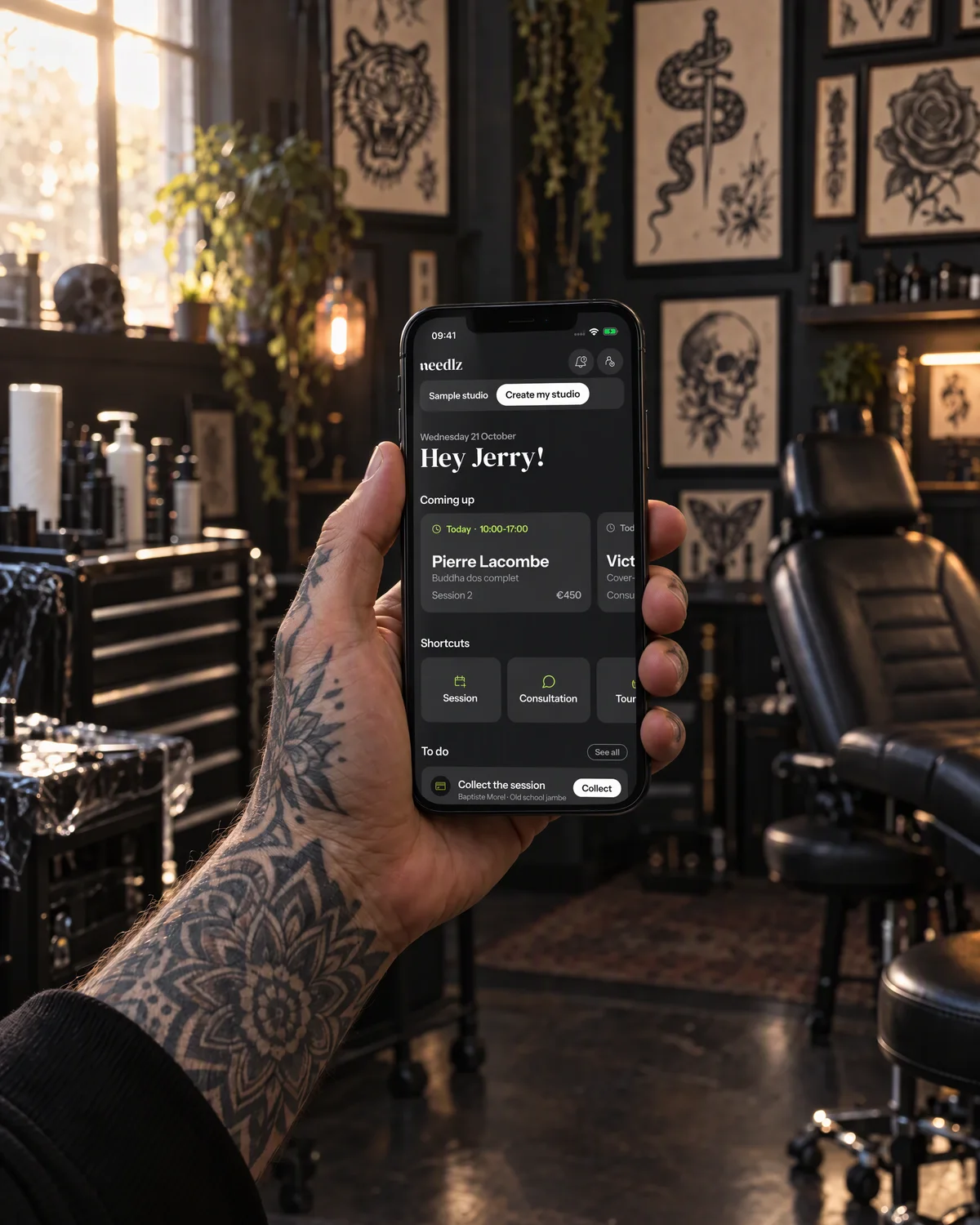 Staged photo: the needlz home screen on an iPhone held by a tattoo artist at the studio