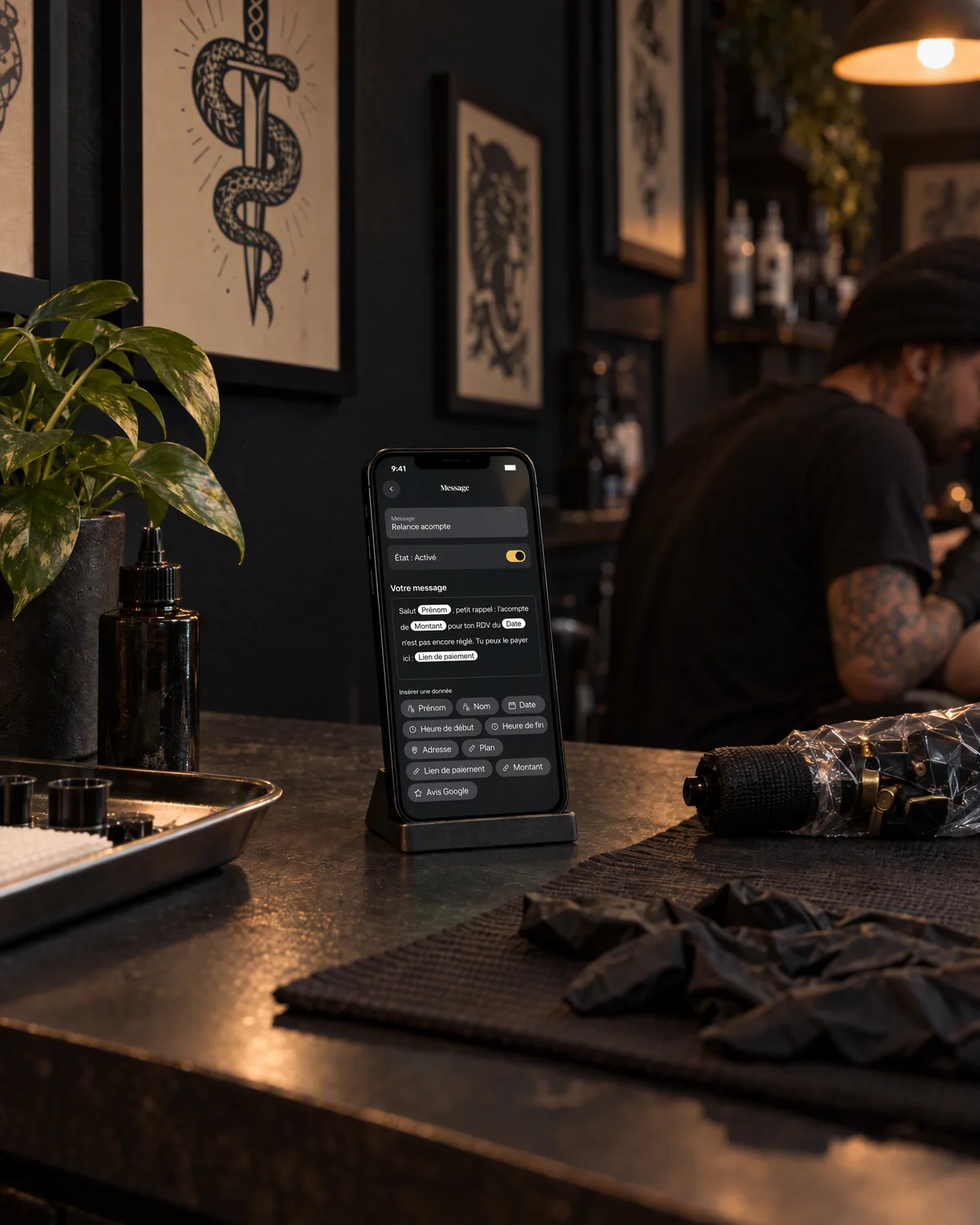 Mise en scène : le message d’acompte de needlz sur un iPhone, à côté d’une machine à tatouer