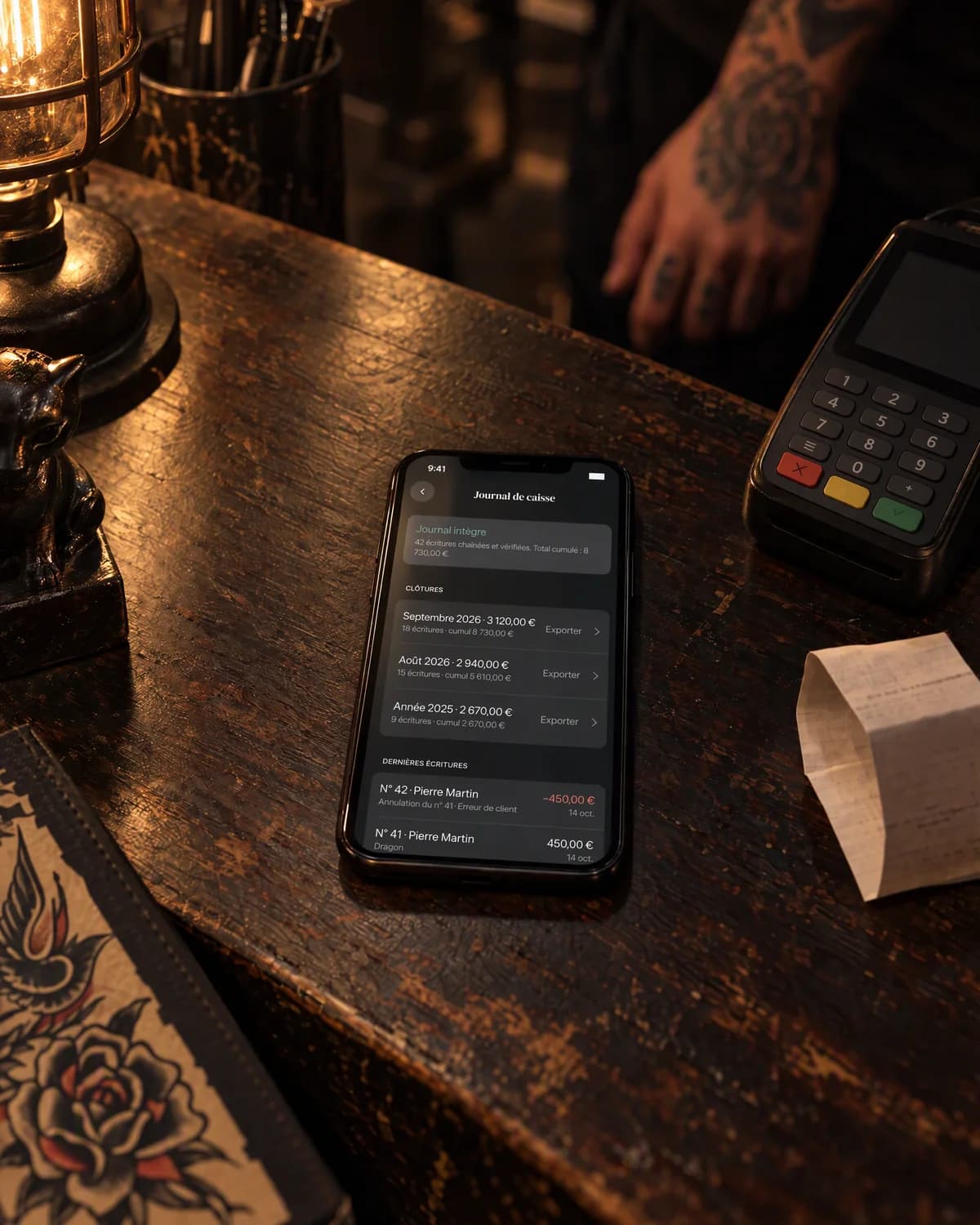 Mise en scène : le journal de caisse de needlz sur un iPhone, à côté d’un terminal de paiement