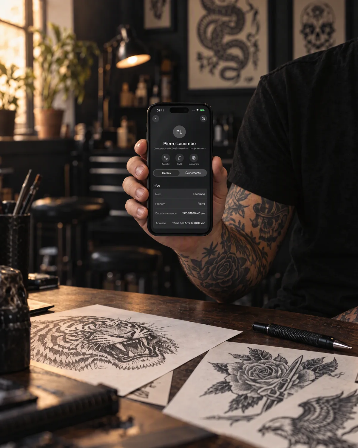 Mise en scène : une fiche client dans needlz, sur un iPhone tenu par un tatoueur